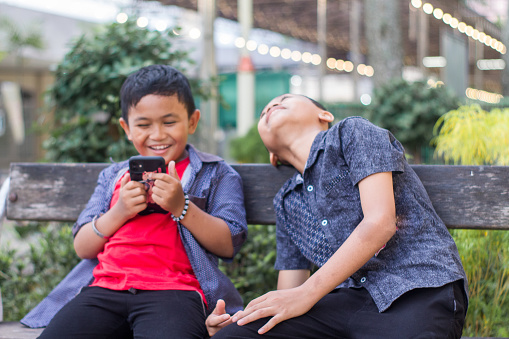 two boys playing smartphone sitting in park