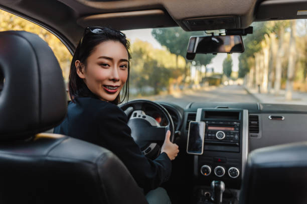 asian woman driving a car and smiling.a young success happy woman is driving a car. - japanese ethnicity women asian and indian ethnicities smiling imagens e fotografias de stock