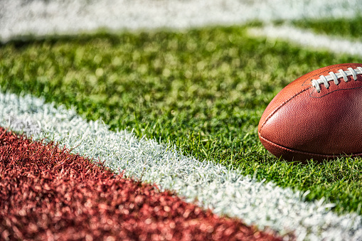 A low angle view of a leather American Football inches from the white goal line of a red end zone.
