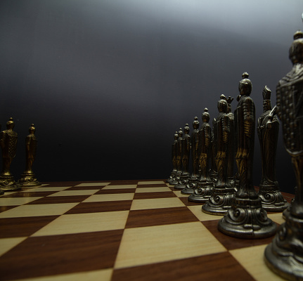 Silver chess figures forming a row on top of a brown and beige wooden chessboard