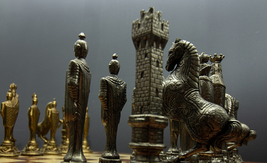 Low angle view of the figures in a chess game with the rook foreground out of focus, a medium shot with knight and bishops in focus and a background with bishops out of focus.