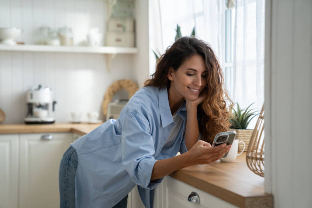 istock Happy pleasant young woman standing in kitchen using smartphone, looking for cooking recipes online 1447958360