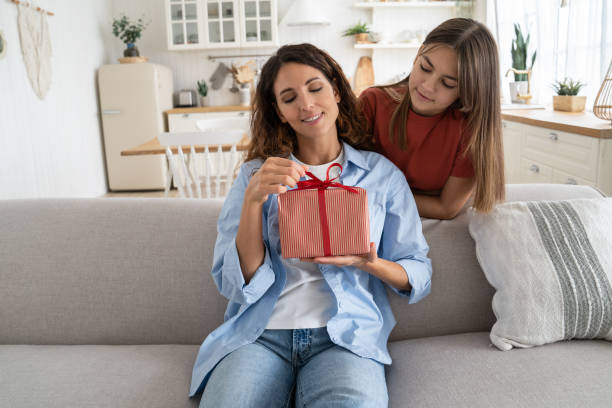 istock Excited young woman mother getting wrapped gift box present from daughter while sitting on sofa 1447959220