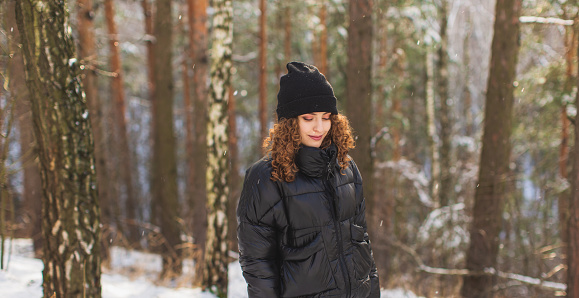 Redhead curly woman in black jacket in winter forest. Warm clothes.