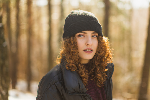 Redhead curly woman in black jacket in winter forest. Warm clothes