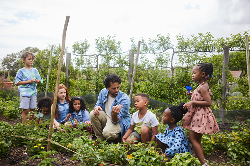 Teacher talking with a group of diverse young student digging in vegetable garden during an outdoor class