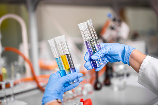 Close up on female laboratory technologist's hands while holding test tubes with colorful liquids during  some new pharmaceutical research.