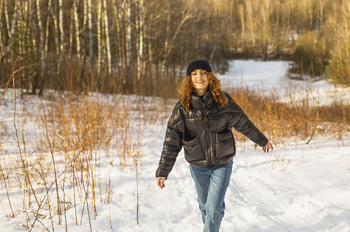 Redhead curly woman in black jacket in winter forest. Warm clothes