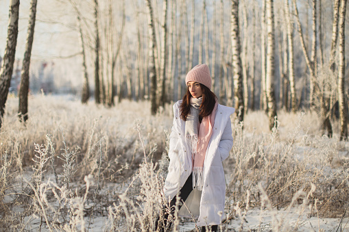 Asian brunette woman in white jacket and scarf in winter forest. Warm clothes.