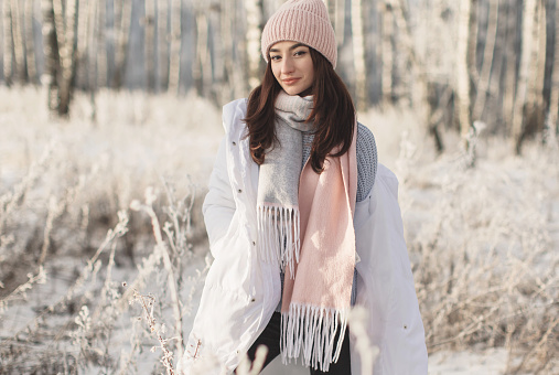 Asian brunette woman in white jacket and scarf in winter forest. Warm clothes