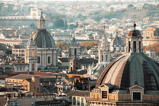 Aerial view of downtown Rome, with plenty of historic buildings and churches topped by ancient domes and bell towers. Autumn season, daylight with atmospheric haze.