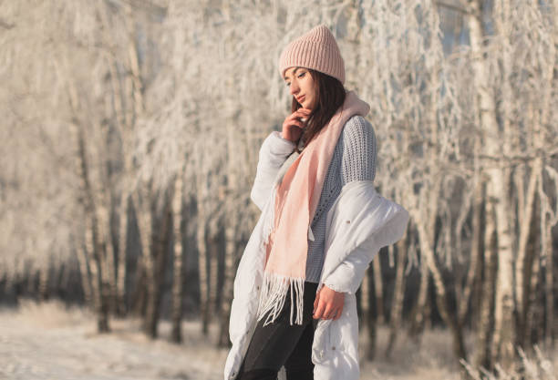 Asian brunette woman in white jacket and scarf in winter forest. Warm clothes. Pretty woman in hat enjoying vacation. Girl in nature. Feel happiness. Hoarfrost and snow on trees
