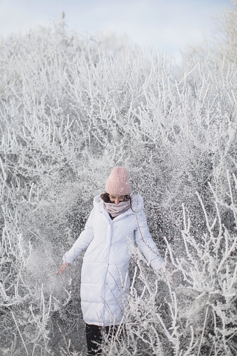 Asian brunette woman in white jacket and scarf in winter forest. Warm clothes