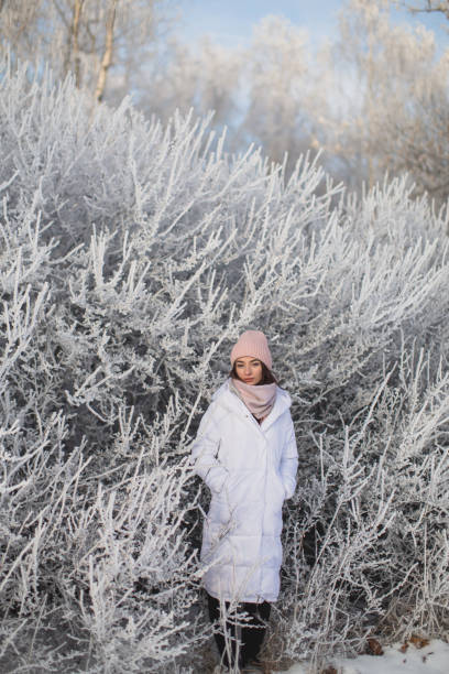 Asian brunette woman in white jacket and scarf in winter forest. Warm clothes