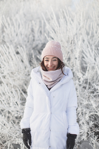 Asian brunette woman in white jacket and scarf in winter forest. Warm clothes