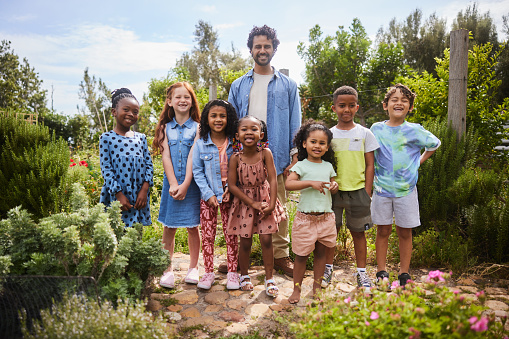 Portrait of a group of diverse young students and a teacher smiling while standing outside in a community vegetable garden