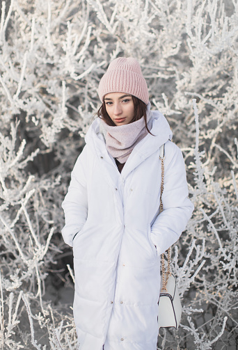 Asian brunette woman in white jacket and scarf in winter forest. Warm clothes.