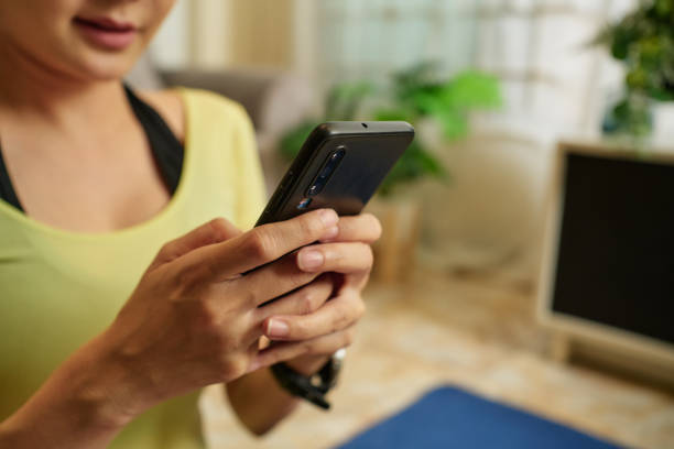 istock Female yoga instructor sitting on yoga mat  input data on Smart phone at home. 1447964704