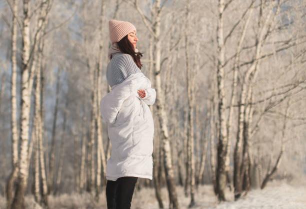Asian brunette woman in white jacket and scarf in winter forest. Warm clothes.