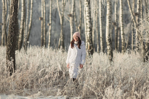 Asian brunette woman in white jacket and scarf in winter forest. Warm clothes