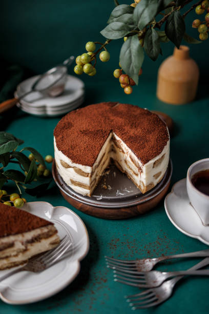 Round tiramisu cake with a slice cut on a teal green background