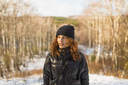Redhead curly woman in black jacket in winter forest