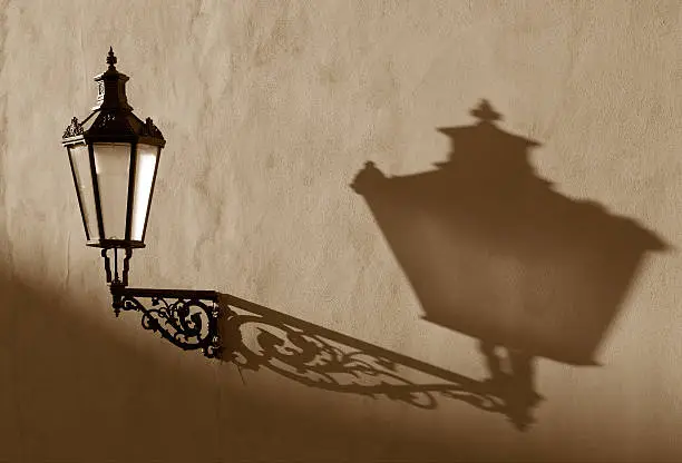 Vintage gas-lamp hanging on the wall casting shadow in low evening sun light, this as well reveals structure on the wall. Location Prague, Czech Republic.