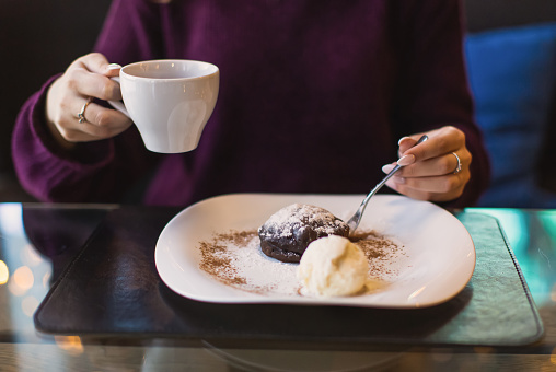 Girl with a cup of coffee in hand. Chocolate brownie dessert with ice cream on plate