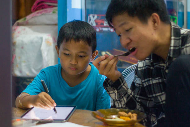 istock Little boy and older brother using tablet phone doing homework while eating 1447969778
