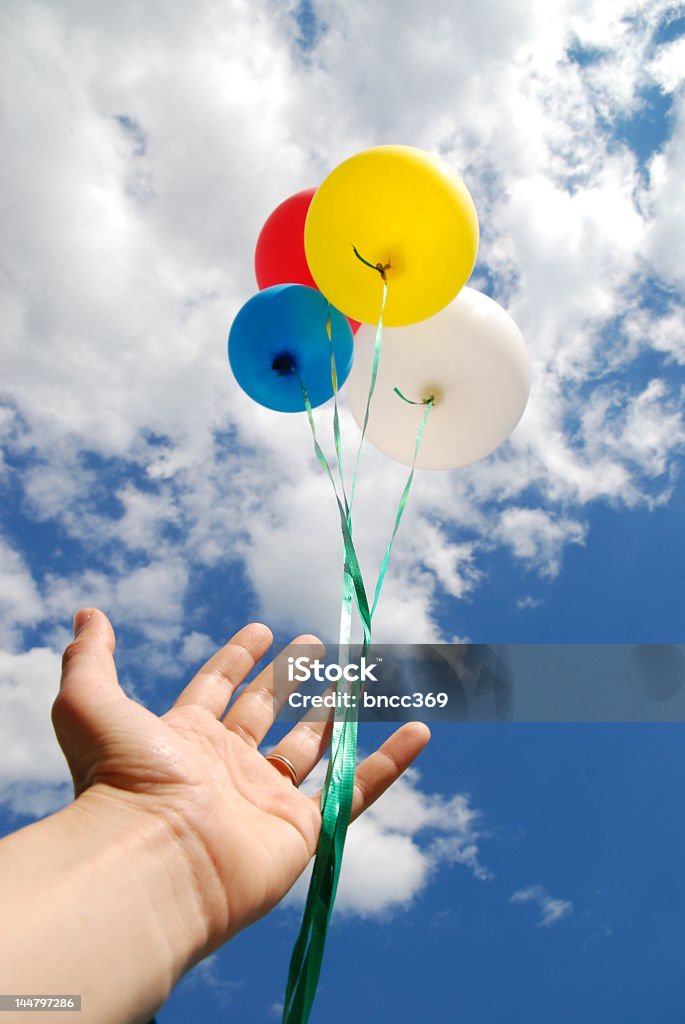 Hand releasing four colorful balloons into the sky Balloons being released into the clouds on a bright summer day. Releasing Stock Photo
