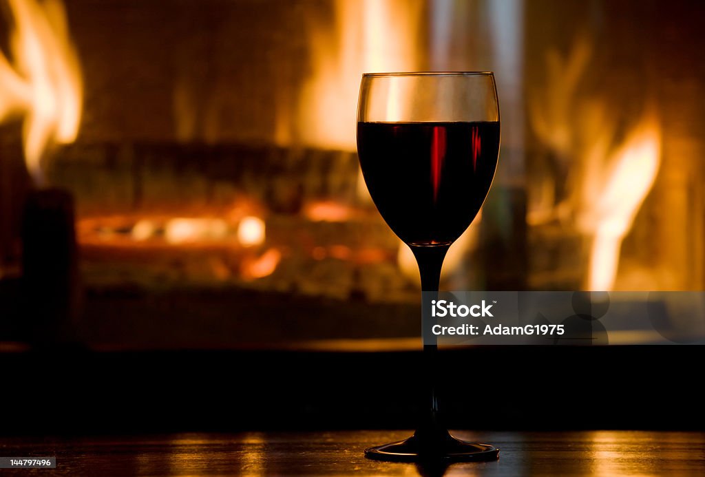 Wineglass Wine glass on wooden table against blazing fireplace. Shallow DOF. Alcohol - Drink Stock Photo