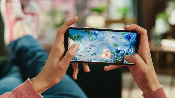 istock Female is Relaxing on a Couch at Home, Playing an Interactive PvP RPG Strategy Video Game on Her Smartphone. Gamer Lies on a Sofa in Living Room. Close Up POV Photo of Mobile Device Screen. 1447975413