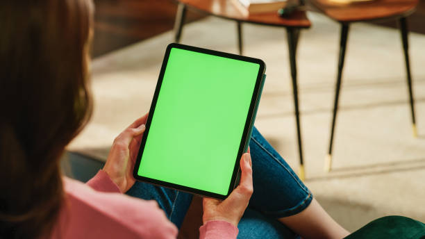 istock Female Scrolling and Tapping on Content on Tablet Computer with Green Screen Mock Up Display. Woman Relaxing at Home, Reading Social Media Posts on Mobile Device. Close Up Over the Shoulder Photo. 1447976505