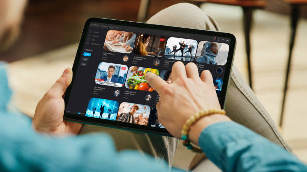 istock Young Handsome Man Using Tablet to Watch Videos on Online Streaming Service. Creative Male Checking Social Media, Browsing Internet, Consuming Content. Urban City View from Big Window. 1447976557