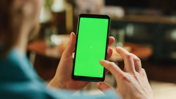 istock Man Scrolling Feed and Double Tapping on Display on Smartphone with Green Screen Mock Up Display. Male Resting at Home, Checking Social Media on Mobile Device. Close Up Over the Shoulder Photo. 1447977366