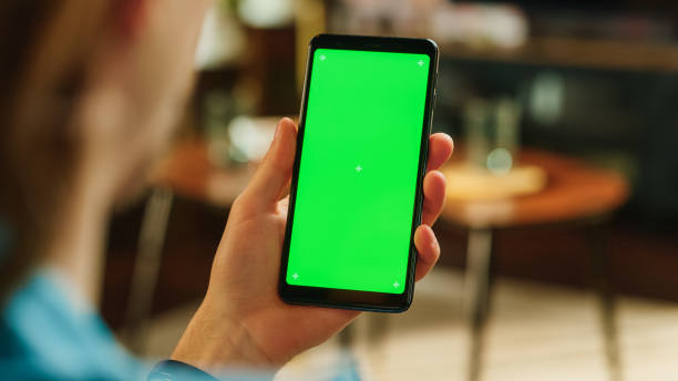 istock Man Swiping on Display and Scrolling Feed on Smartphone with Green Screen Mock Up Display. Male Resting at Home, Checking Social Media on Mobile Device. Close Up Over the Shoulder Photo. 1447977393