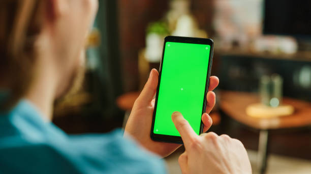 istock Man Scrolling Feed on Smartphone with Green Screen Mock Up Display. Male Having Fun and Enjoying Content on Social Media on Mobile Device while Resting at Home. Close Up Over the Shoulder Photo. 1447977398