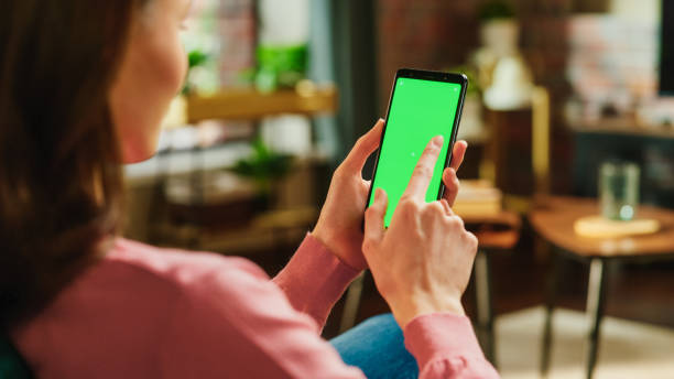 istock Feminine Hand Tapping on Display and Scrolling Feed on Smartphone with Green Screen Mock Up Display. Female Resting at Home, Checking Social Media on Mobile Device. Close Up Over the Shoulder Photo. 1447977434