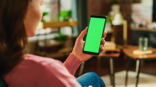 istock Feminine Hand Tapping on Display and Scrolling Feed on Smartphone with Green Screen Mock Up Display. Female Resting at Home, Checking Social Media on Mobile Device. Close Up Over the Shoulder Photo. 1447977439