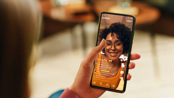 main féminine tenant un smartphone avec l’application de médias sociaux sur l’écran. femme en vêtements décontractés se reposant à la maison et regardant des vidéos sur un appareil mobile. gros plan au-dessus de la photo d’épaule. - influenceur photos et images de collection