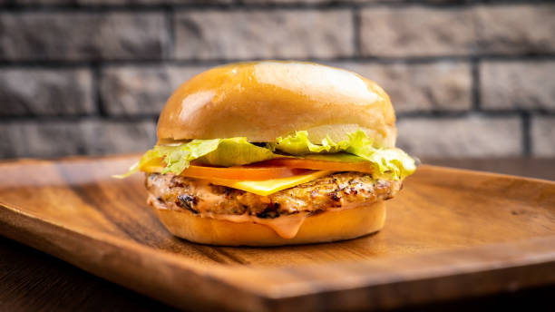 istock Chicken burger with cheese salad, tomato and leaf isolated on wooden board side view on table fast food 1447982705