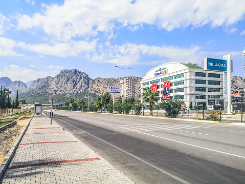 Antalya, Turkey - October 27, 2019: View of the mountain landscape and Okyanus Koleji from Akdeniz Bulvari street in Antalya. An empty boulevard in a Turkish city with a highway in the foreground