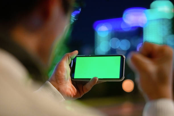 Excited man holding smartphone outdoors in night city