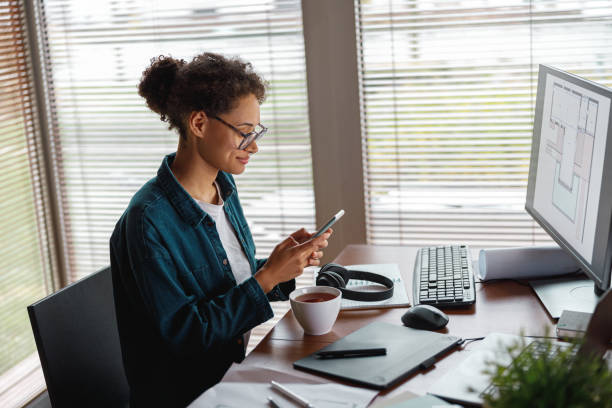 улыбающаяся женщина-дизайнер интерьера держит смартфон во время перерыва в домашнем офисе. концепция фриланса - digital tablet digitized pen laptop black стоковые фото и изображения