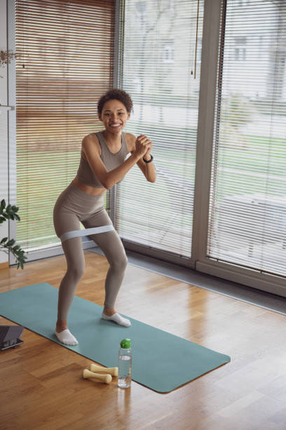 istock Slim woman doing exercises for legs with elastic band by online tutorials on laptop in living room 1448004497