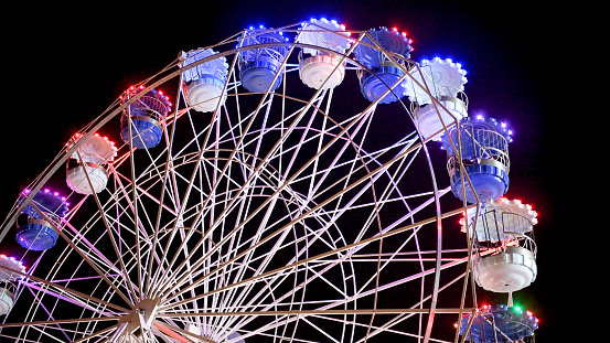 Colourful striped light illuminated spinning ferris wheel in motion moving at night.