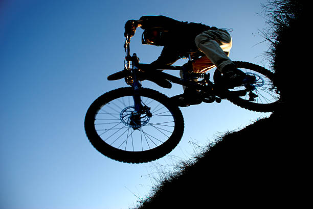 A male downhill mountain biker sprays rocks in the air while making a turn at sunset.