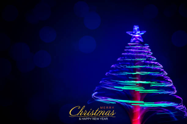 Christmas greeting. Spinning Christmas tree made of fiber optics (motion blurred). Dark blue background with bokeh lights. Merry Christmas and Happy New Year text.