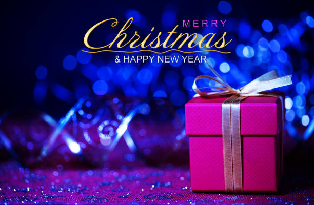 Close-up of a Christmas present (gift box) with defocused Christmas lights and decorations in the background. Merry Christmas and Happy new year text.