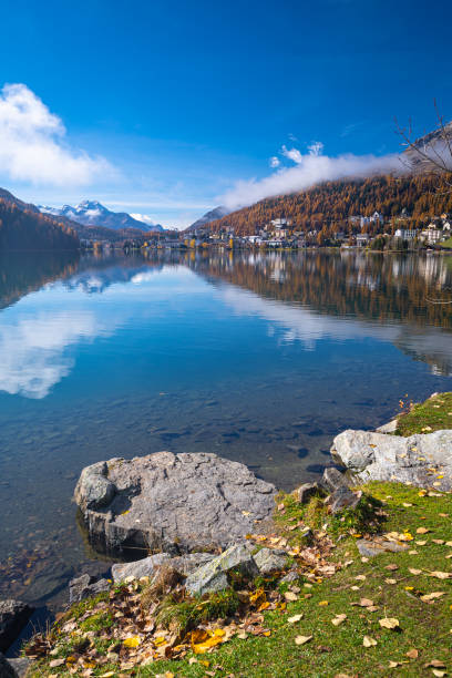 Serene image of Lake Saint Moritz in Engadin valley with gold colored larches on the mountain slopes.
